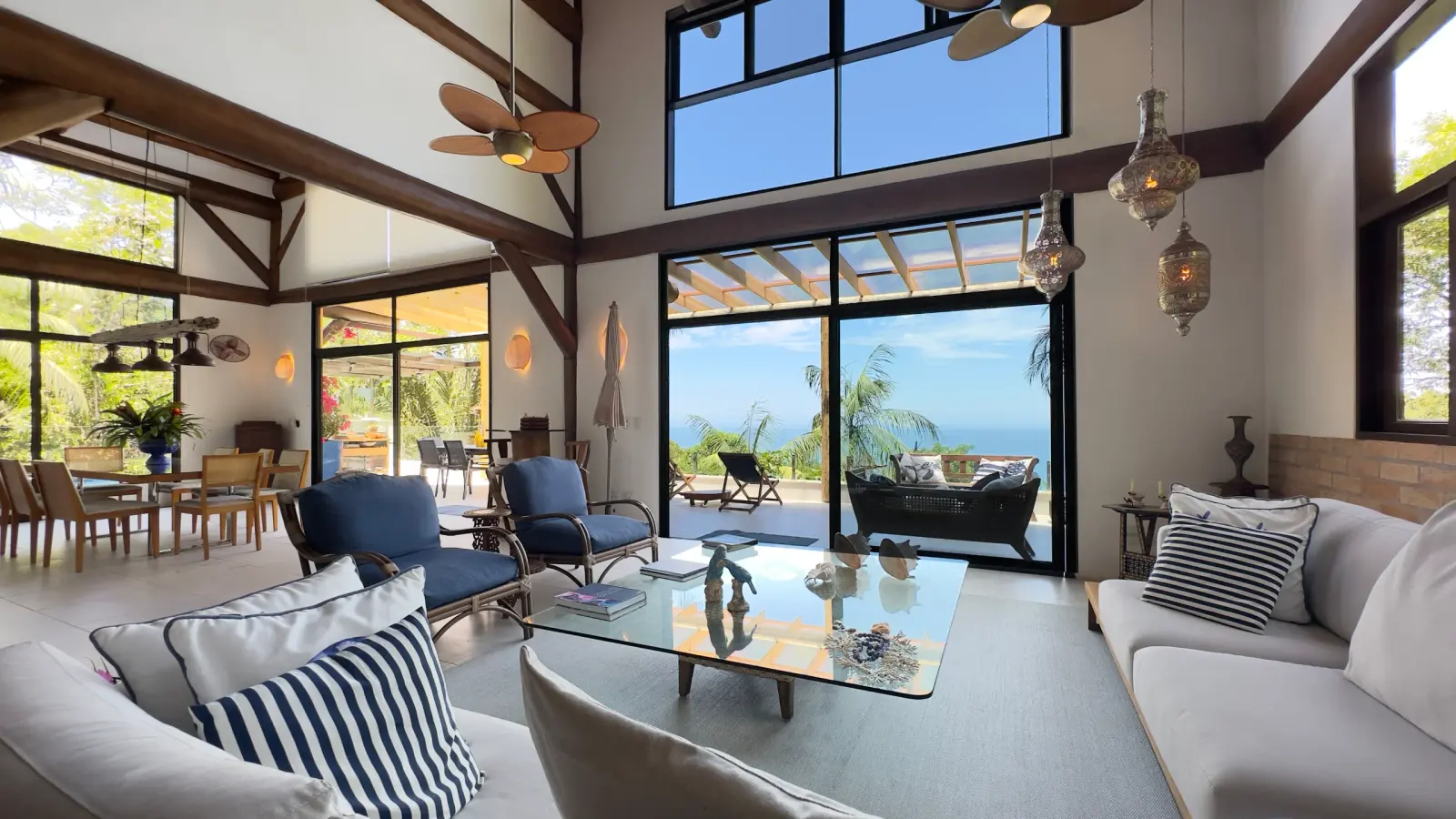 Sala de estar da Villa 231 com pé-direito duplo, grandes janelas e vista para o mar no Condomínio Iporanga.