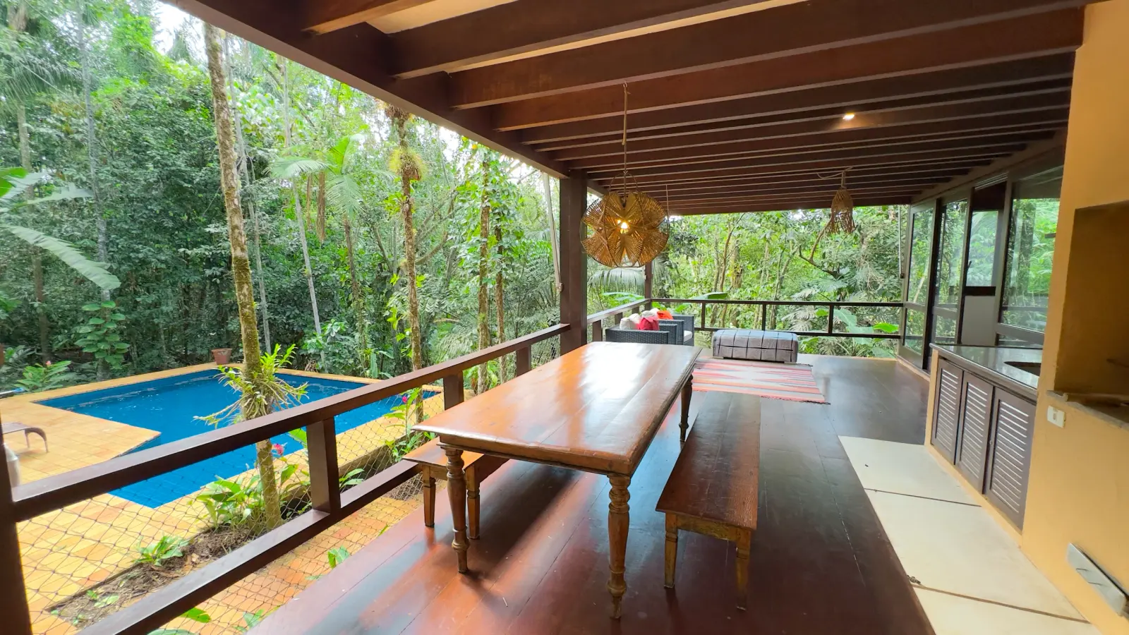 Villa 411 - Casa à venda Condominio Iporanga - Mesa da varanda externa com luminaria de teto estilizada, piscina aos fundos à esquerda e amplitude da varanda