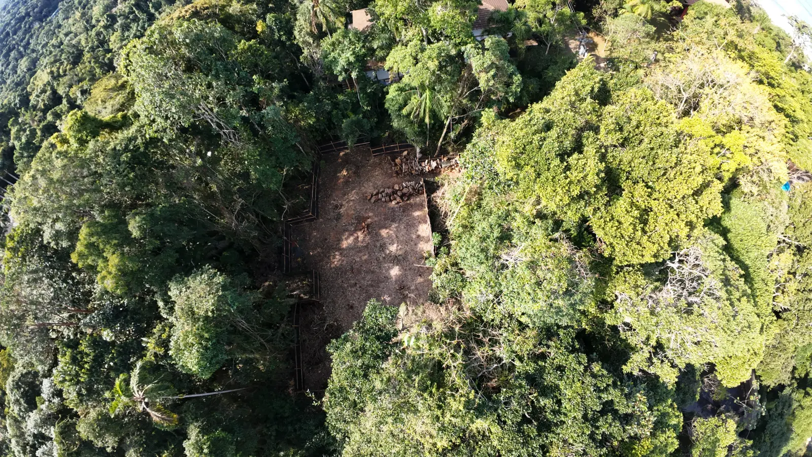 Foto com detalhe de terreno desmatado e vista aérea da mata atlantica da serra do gauraru que cerca o terreno